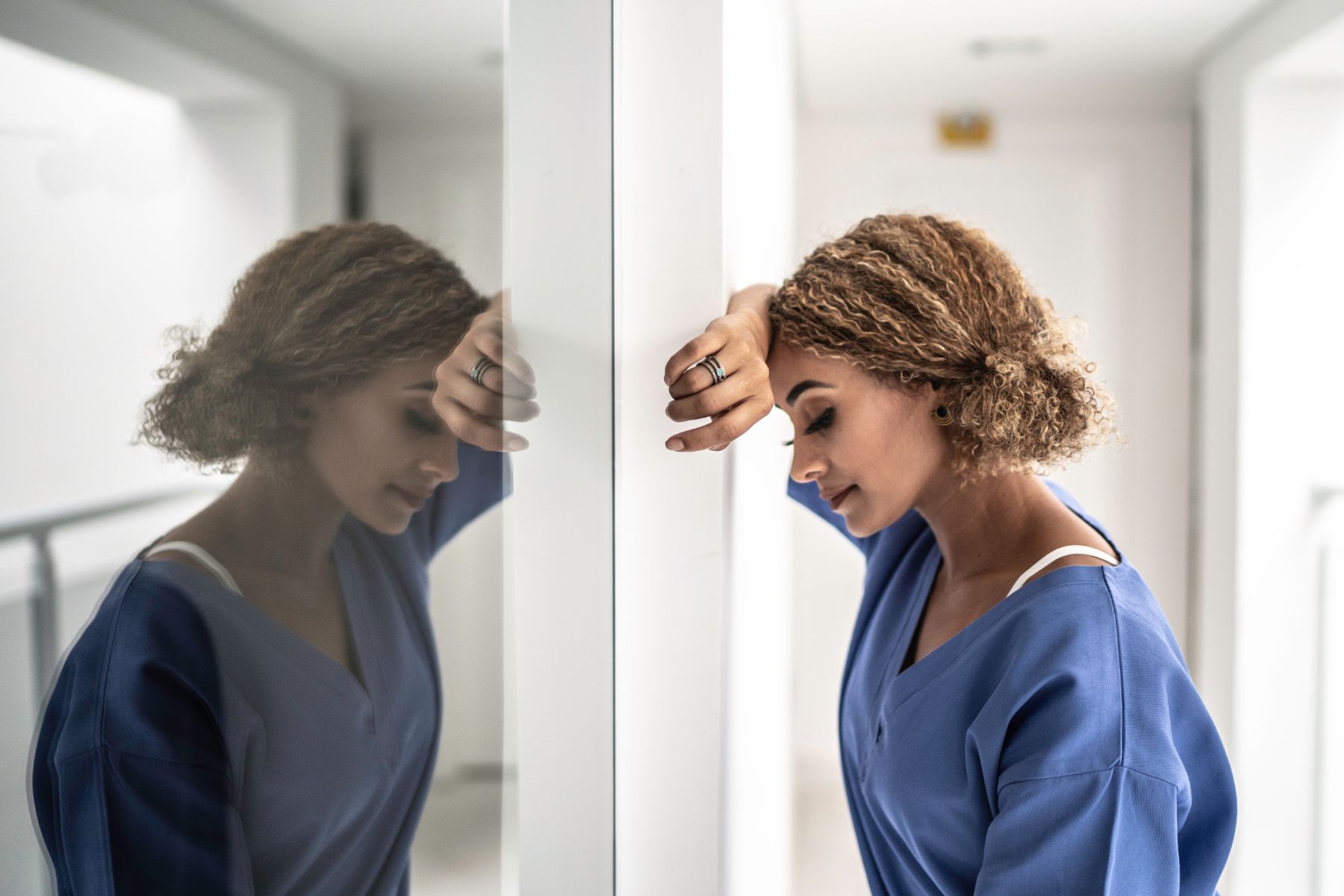 burn out nurse leaning against glass with reflection